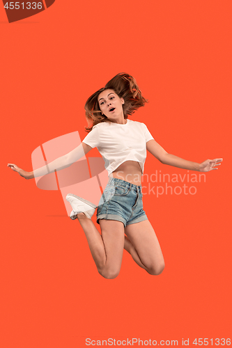 Image of Freedom in moving. Pretty young woman jumping against orange background