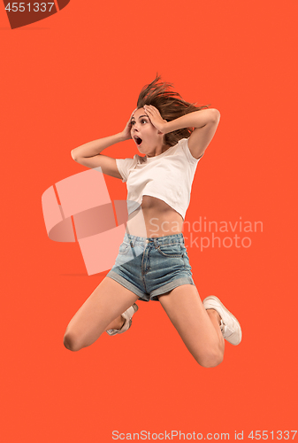 Image of Freedom in moving. Pretty young woman jumping against orange background