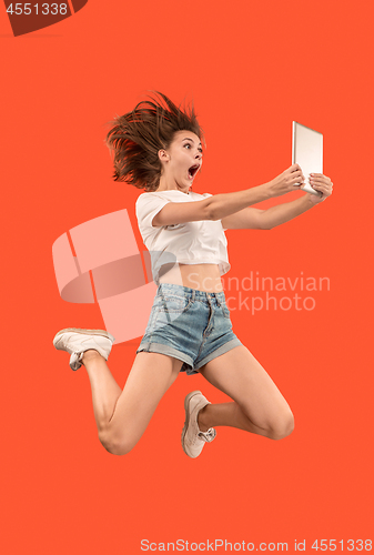 Image of Image of young woman over red background using laptop computer or tablet gadget while jumping.