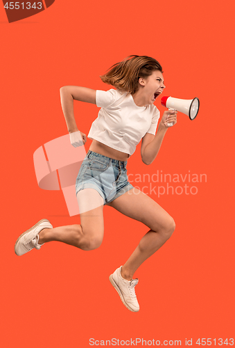 Image of Beautiful young woman jumping with megaphone isolated over red background