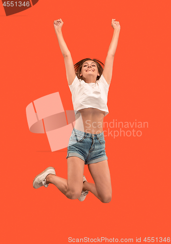 Image of Freedom in moving. Pretty young woman jumping against orange background