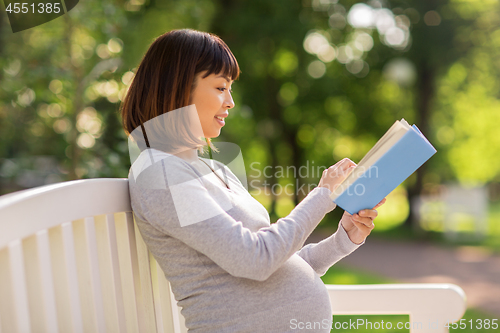 Image of happy pregnant asian woman reading book at park