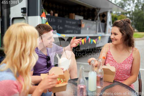 Image of happy friends with drinks eating at food truck