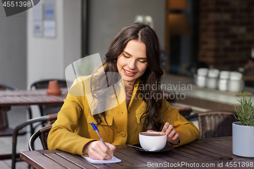 Image of happy woman with notebook drinking cocoa at cafe