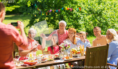 Image of happy family photographing at dinner in garden