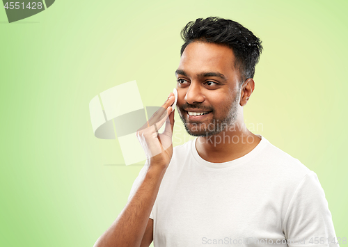 Image of smiling indian man cleaning face with cotton pad