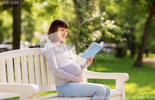 Image of happy pregnant asian woman reading book at park