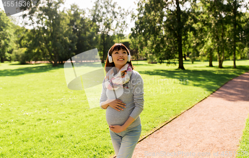 Image of happy pregnant asian woman in headphones at park