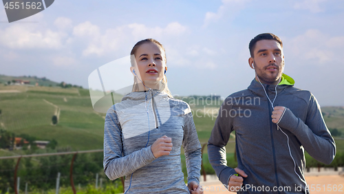 Image of happy couple with earphones running outdoors