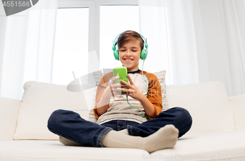 Image of happy boy with smartphone and headphones at home