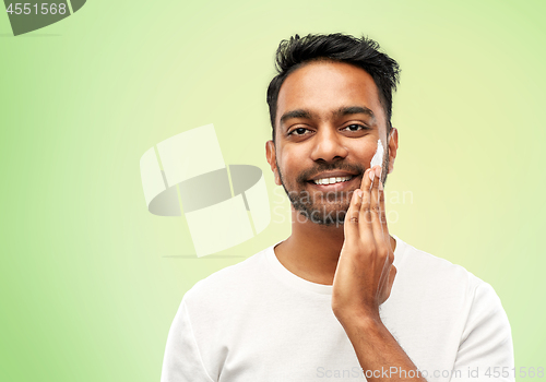 Image of happy indian man applying cream to face