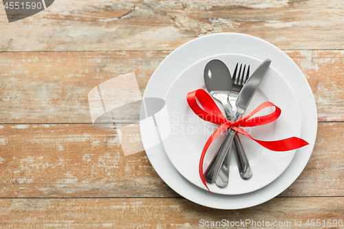 Image of cutlery tied with red ribbon on set of plates