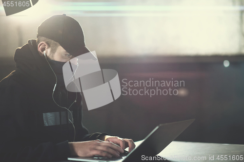 Image of young talented hacker using laptop computer while working in dar