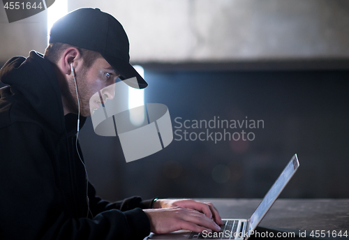 Image of talented hacker using laptop computer while working in dark offi