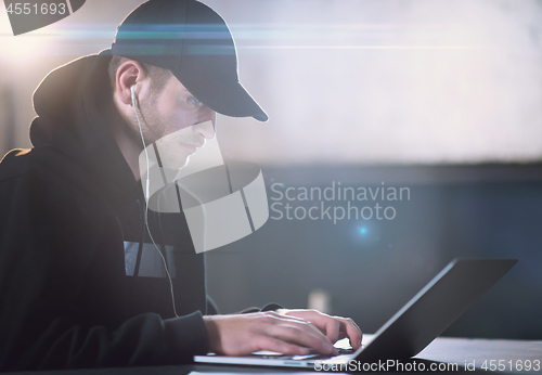 Image of young talented hacker using laptop computer while working in dar