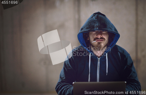 Image of young hacker using laptop computer while working in dark office