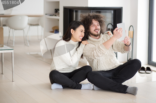 Image of multiethnic couple using tablet computer in front of fireplace