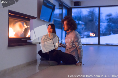 Image of happy multiethnic couple sitting in front of fireplace