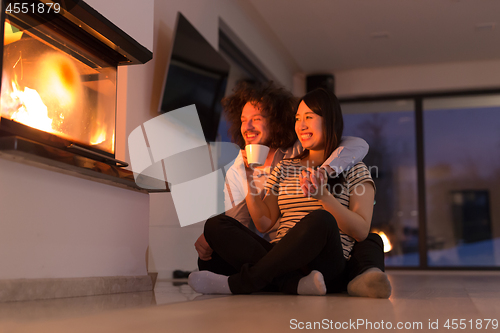 Image of happy multiethnic couple sitting in front of fireplace