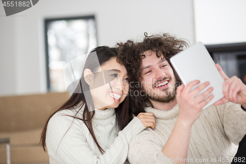 Image of multiethnic couple using tablet computer in front of fireplace