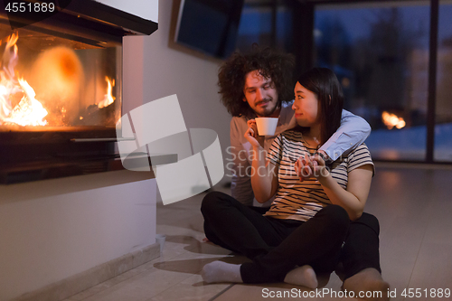 Image of happy multiethnic couple sitting in front of fireplace