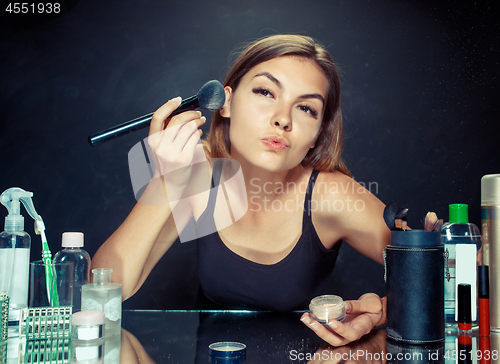 Image of Beauty woman applying makeup. Beautiful girl looking in the mirror and applying cosmetic with a big brush.