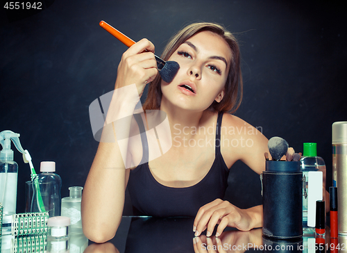 Image of Beauty woman applying makeup. Beautiful girl looking in the mirror and applying cosmetic with a big brush.