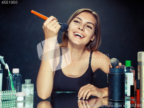 Image of Beauty woman applying makeup. Beautiful girl looking in the mirror and applying cosmetic with a big brush.
