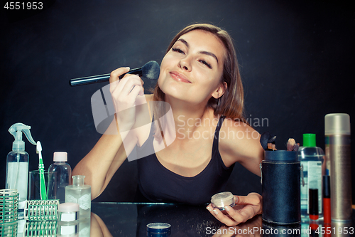 Image of Beauty woman applying makeup. Beautiful girl looking in the mirror and applying cosmetic with a big brush.