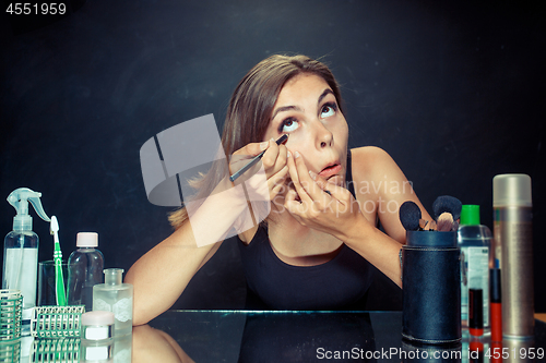 Image of Beauty woman applying makeup. Beautiful girl looking in the mirror and applying cosmetic with a brush.