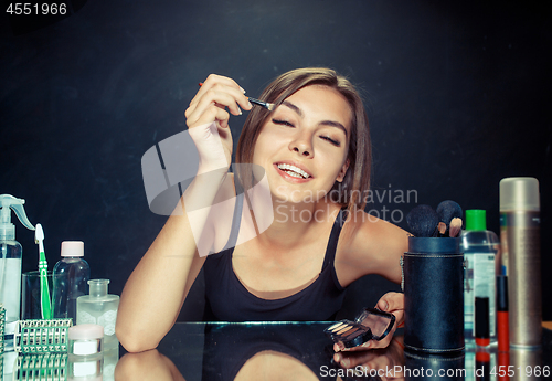 Image of Beauty woman applying makeup. Beautiful girl looking in the mirror and applying cosmetic with a brush.