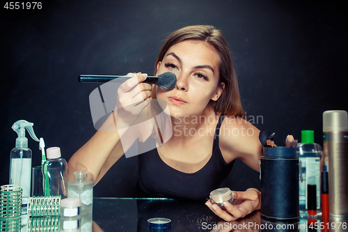 Image of Beauty woman applying makeup. Beautiful girl looking in the mirror and applying cosmetic with a big brush.