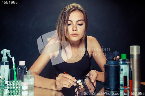 Image of Beauty woman applying makeup. Beautiful girl looking in the mirror and applying cosmetic with a brush.