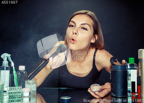 Image of Beauty woman applying makeup. Beautiful girl looking in the mirror and applying cosmetic with a big brush.