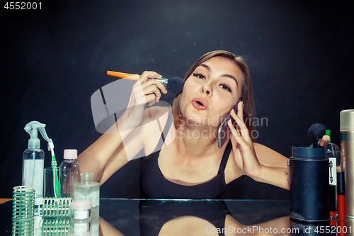 Image of Beauty woman applying makeup. Beautiful girl looking in the mirror and applying cosmetic with a big brush.