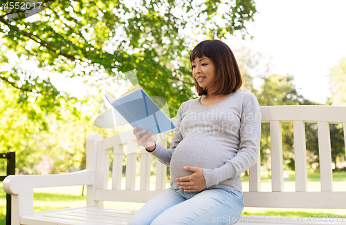 Image of happy pregnant asian woman reading book at park