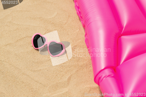 Image of sunglasses and pink swimming mattress on beach