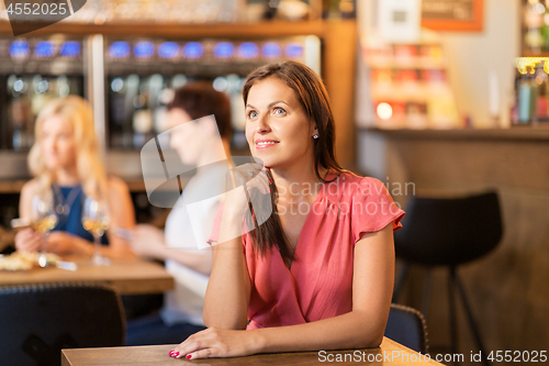 Image of happy middle aged woman at wine bar or restaurant