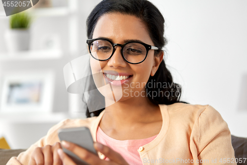 Image of happy indian woman using smartphone at home