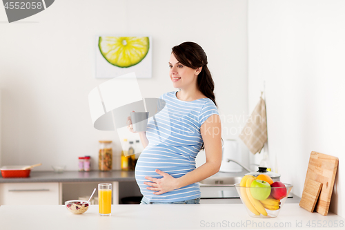 Image of happy pregnant woman with cup at home kitchen