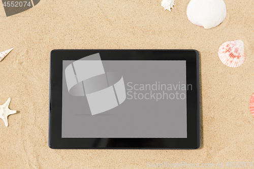 Image of tablet computer and seashells on beach sand