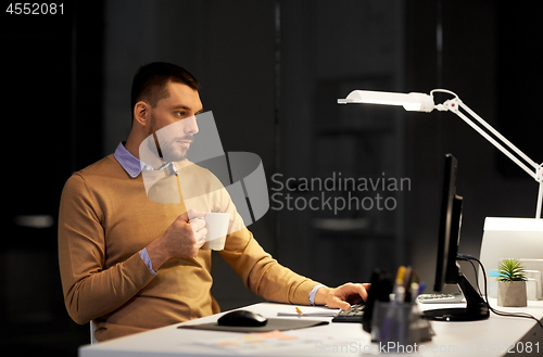 Image of man with laptop and coffee working at night office