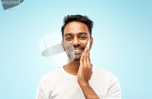 Image of happy indian man applying cream to face