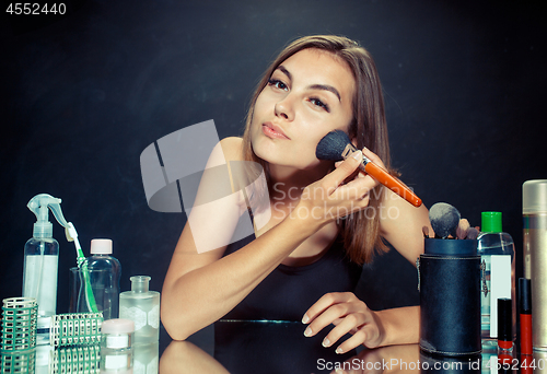 Image of Beauty woman applying makeup. Beautiful girl looking in the mirror and applying cosmetic with a big brush.