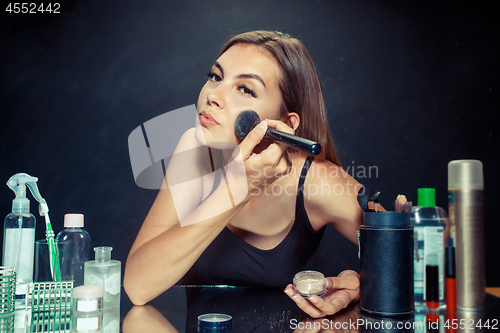 Image of Beauty woman applying makeup. Beautiful girl looking in the mirror and applying cosmetic with a big brush.