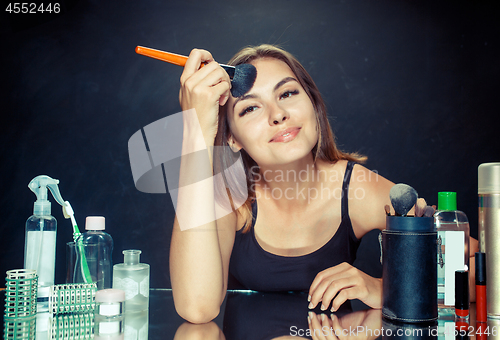 Image of Beauty woman applying makeup. Beautiful girl looking in the mirror and applying cosmetic with a big brush.