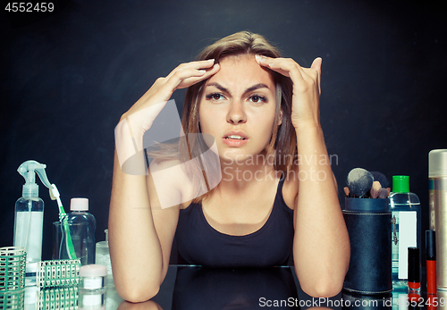 Image of Unsatisfied young woman looking at her self in mirror on black background