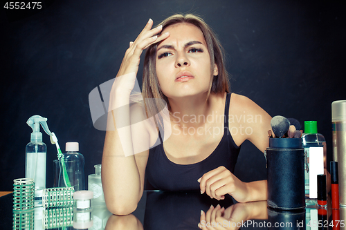 Image of Unsatisfied young woman looking at her self in mirror on black background