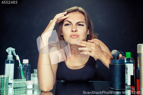 Image of Unsatisfied young woman looking at her self in mirror on black background