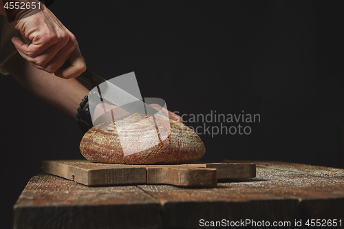 Image of man slicing fresh organic bread on wooden board